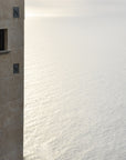 Stone building with arched window and square windows overlooking a vast calm ocean