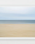 Framed artwork of an abstract beach scene with a blue sky and beige, yellow sand.