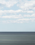 Wide abstract expanse of ocean meeting a clear blue sky with scattered clouds