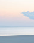 This image captures a serene and abstract view of a sunset cloud over Chatham, Cape Cod. The backdrop features a calm sea and a sky busting with light, with a prominent cloud silhouetted against the fading sun and pink sky