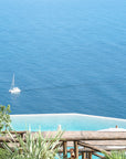 This image displays a framed artwork titled "Sailing the Tyrrhenian Sea," featuring a serene scene of a sailboat gently floating on the expansive, clear blue waters of the Tyrrhenian Sea. The composition includes a bird's-eye view of the boat, providing a sense of its small size in comparison to the boundless sea.
