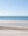 An abstract photograph of a beach scene with horizontal lines defined by the sea and sand, under a clear blue sky.