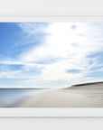 This image presents a framed artwork titled "Lighthouse Beach," featuring a serene and expansive beach scene. The photograph captures the tranquil waters of the ocean meeting the sandy shores under a wide, open sky filled with soft, billowing clouds.