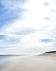 This image presents a framed artwork titled "Lighthouse Beach," featuring a serene and expansive beach scene. The photograph captures the tranquil waters of the ocean meeting the sandy shores under a wide, open sky filled with soft, billowing clouds in Chatham, Cape Cod