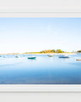 This image displays a framed artwork titled "Cohasset Harbor," capturing the serene and picturesque view of a harbor in Cohasset, Massachusetts. The photograph features a broad expanse of calm blue water, gently扰led by the setting sun, and is dotted with several small boats.