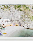 A seaside cove with clear water, white sandy beach and a small fishing village with colorful boats on the Italian coast