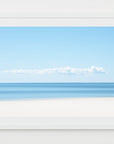 This image displays a captivating artwork titled "Long Cloud, Cape Cod," which features a serene and expansive view of the Cape Cod shoreline. The artwork captures the still ocean meeting a lightly clouded blue sky, accentuated by a prominent, elongated cloud formation stretching across the mid-sky.