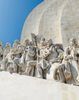 Stone sculpture of historical figures in Lisbon against a vibrant blue sky