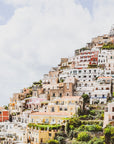 A scenic view of a town with multicolored houses built on a hillside, with the sea in the foreground and a clear blue sky in the background.