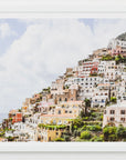 A scenic view of a town with multicolored houses built on a hillside, with the sea in the foreground and a clear blue sky in the background.