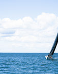 Sailboat with large black sail on the ocean with cloudy sky