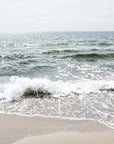 This image presents an artwork titled "Shore Thing," featuring a serene beach scene with the calming waves of the ocean meeting the sandy shore. The photograph highlights the natural beauty of Harwich Port on Cape Cod.