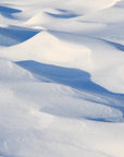 A snowy landscape featuring drifted snow with visible wave-like patterns.