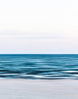 This image presents an abstract photograph titled "End of the Day," featuring a serene beach scene. The photograph captures the tranquil ocean meeting the shore under a soft, overcast sky with blue and pink undertones.