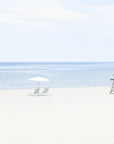 This image presents a framed artwork titled "Time to Chill," featuring a serene beach scene. The artwork captures a calm ocean meets a sandy shore lined with beach umbrellas and a lifeguard tower, suggesting a sense of relaxation and leisure.