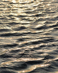 This image features a captivating photograph titled "Water Glow," showcasing the serene and expansive Atlantic Ocean. The artwork captures the texture and subtle colors of the ocean surface, enhanced by a soft, golden light that Imparts a tranquil and almost ethereal quality to the scene.
