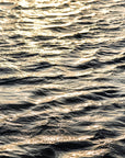 This image features a captivating photograph titled "Water Glow," showcasing the serene and expansive Atlantic Ocean. The artwork captures the texture and subtle colors of the ocean surface, enhanced by a soft, golden light that Imparts a tranquil and almost ethereal quality to the scene.