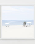 This image presents a framed artwork titled "Time to Chill," featuring a serene beach scene. The artwork captures a calm ocean meets a sandy shore lined with beach umbrellas and a lifeguard tower, suggesting a sense of relaxation and leisure.