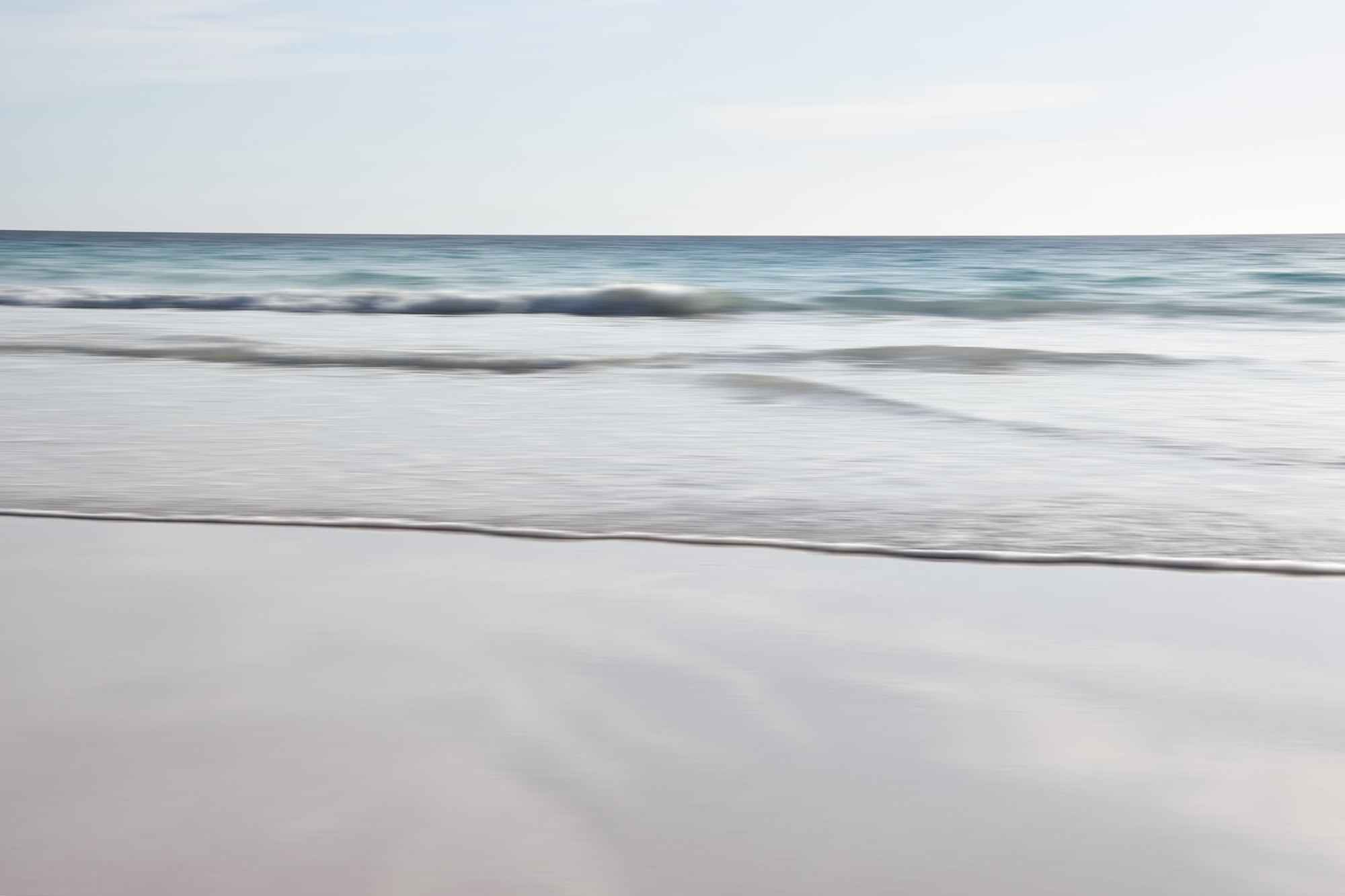 A serene abstract beach scene with gentle waves and a clear sky. Soft blue, grey, pink and beige under tones