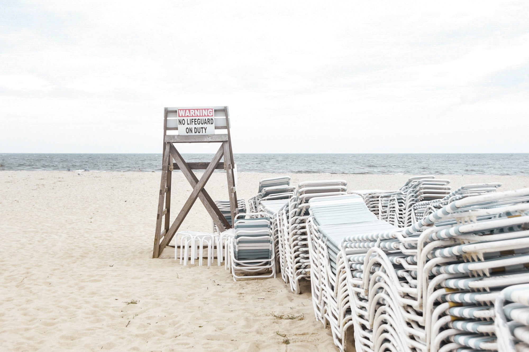 Beach scene with stacked chairs and a lifeguard stand on a sandy beach at Wychmere Beach Club
