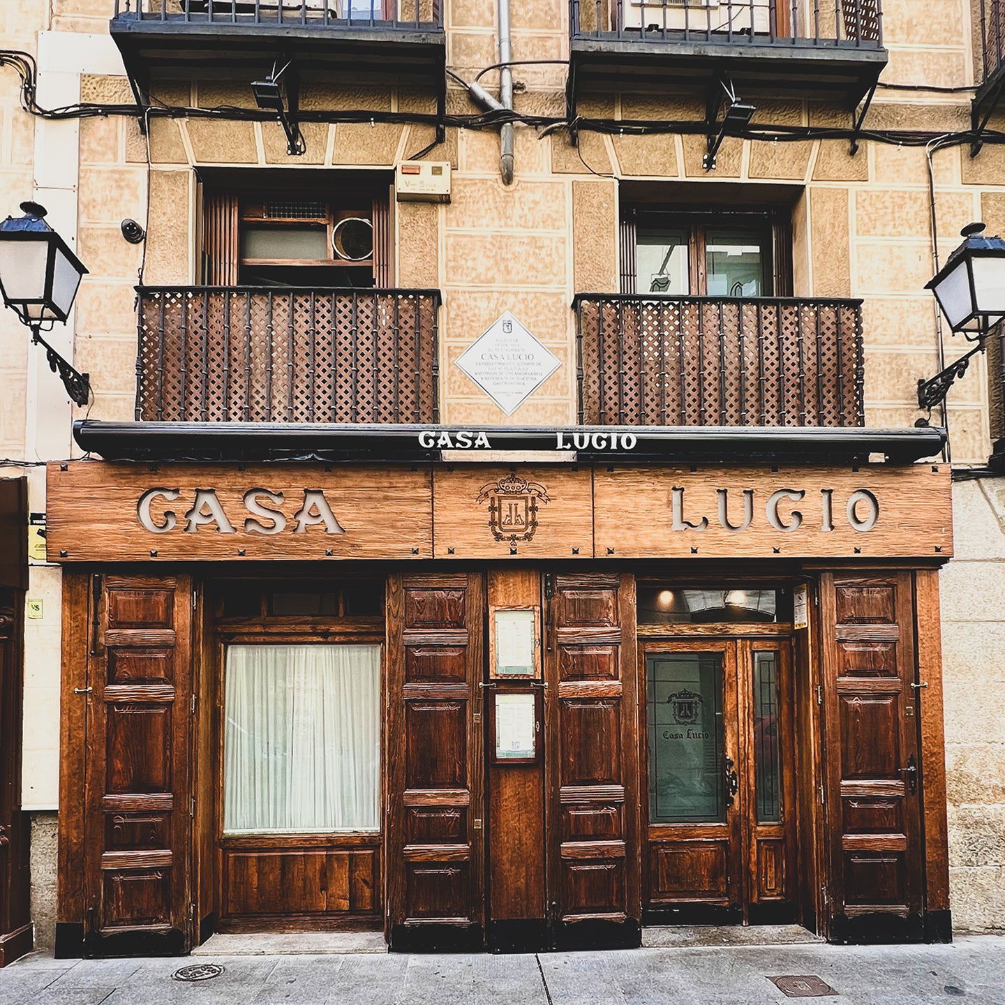 A front view of a building with a sign that reads 'CASA LUCIO' above the entrance. The building has a wooden facade and a black balcony on the upper floor.