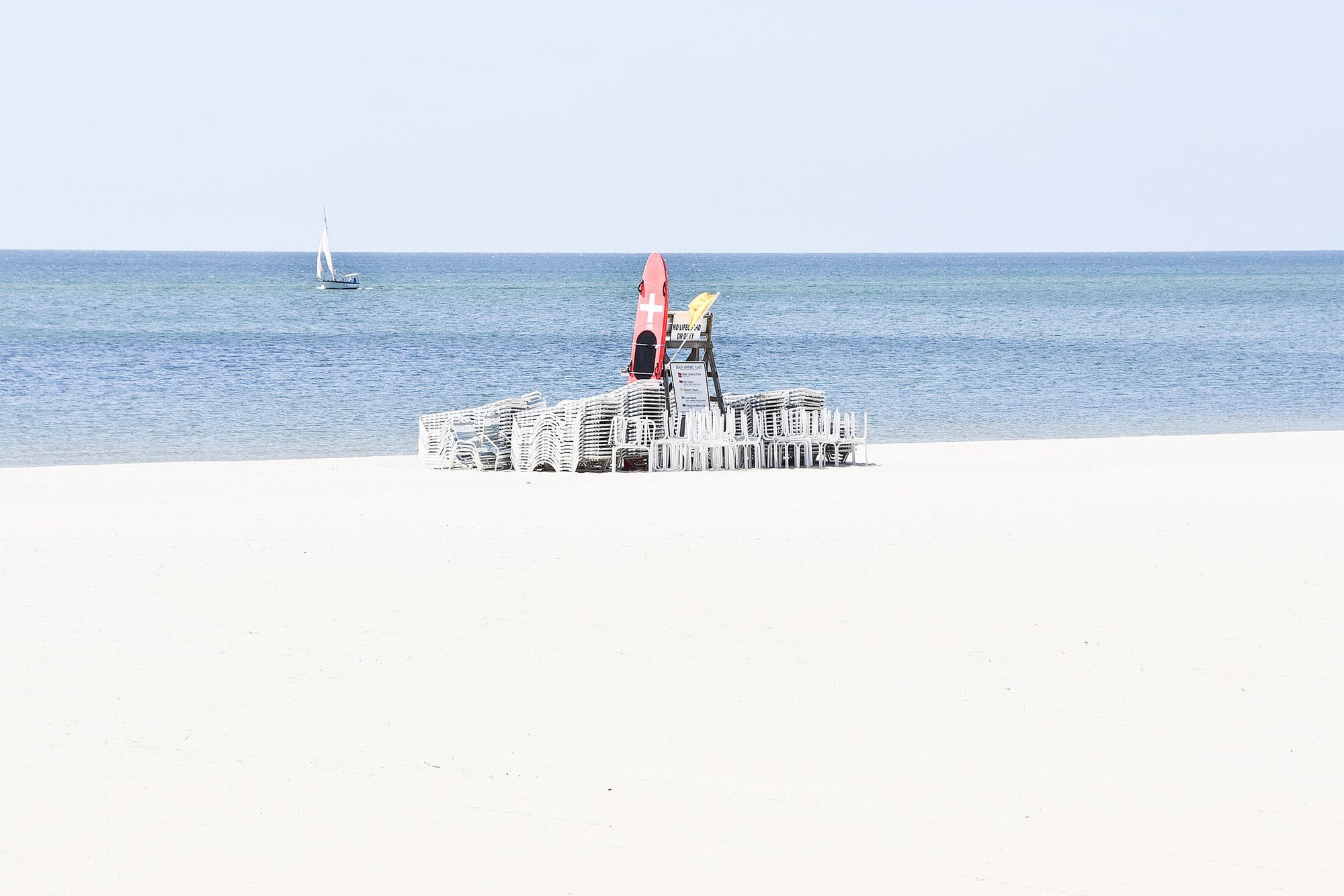 Life guard chair on a sandy beach with clear blue sky and ocean.