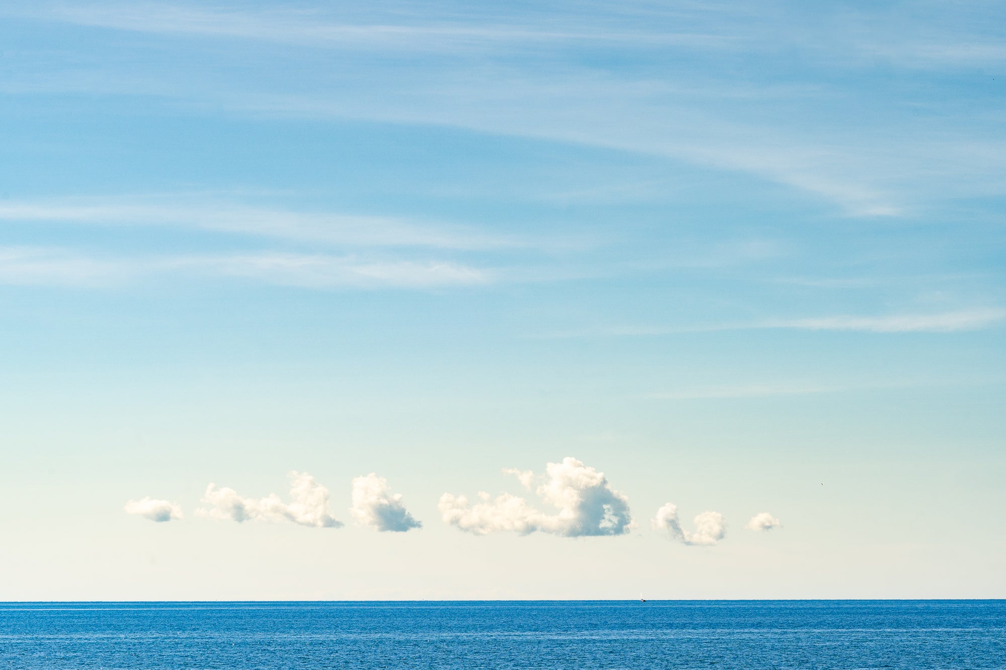 Clear blue sky with a few scattered clouds over a calm ocean.