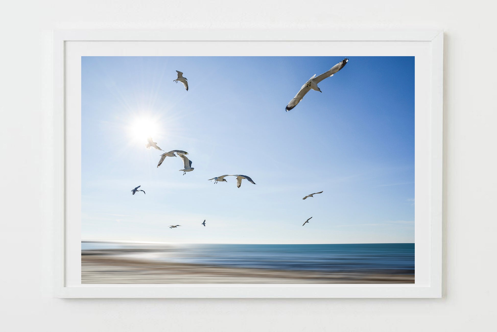 Framed artwork of seagulls flying over a beach with a blue sky.