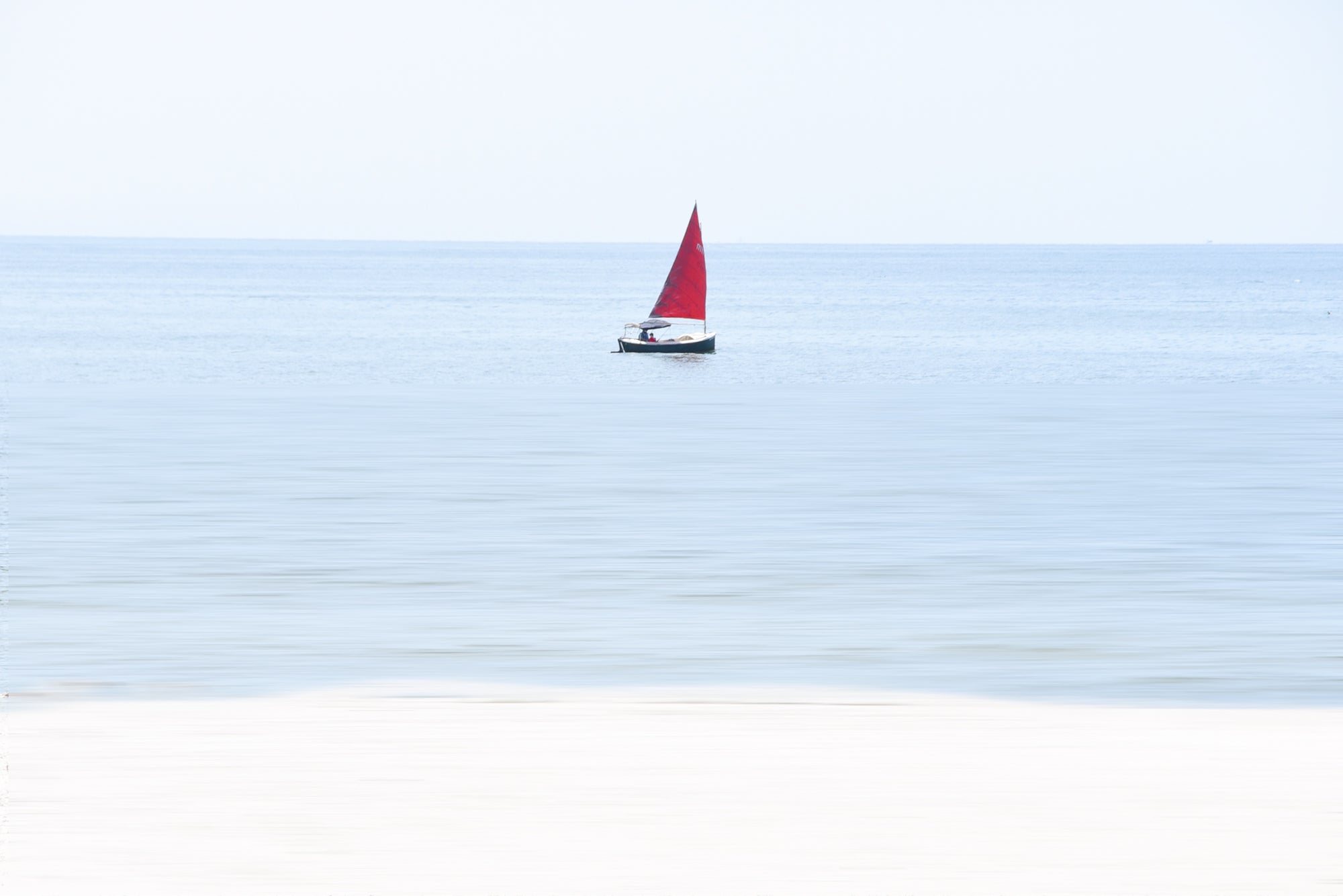 Sailboat with a red sail on a calm blue ocean